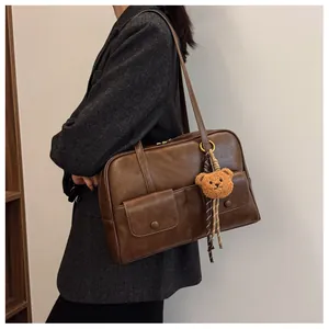 Detail view of brown vintage shoulder bag with two front pockets and a cute bear charm