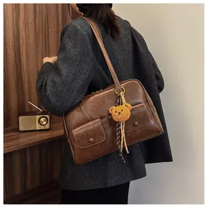 Close-up of vintage brown leather shoulder bag with side pockets and plush bear charm