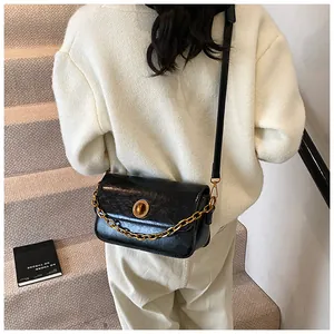 Close-up of black glossy patent leather shoulder bag with gold chain and round clasp