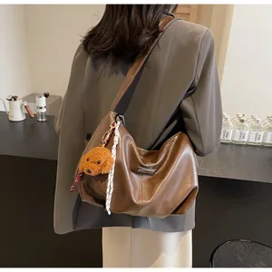 Sac fourre-tout hobo en cuir marron avec charme nounours porté à l'épaule