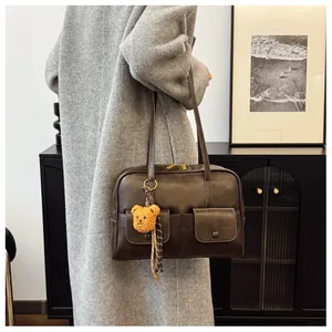 Detail view of a retro dark brown shoulder bag featuring dual front buckle pockets and bear charm