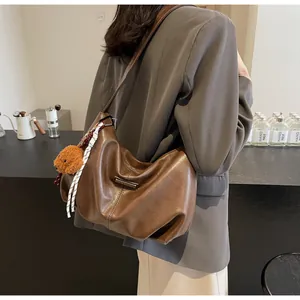Détail du sac hobo en cuir marron foncé avec breloque ours en peluche et ruban rayé