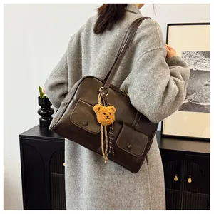 Detail view of dark brown leather shoulder bag featuring front pockets and bear charm accessory