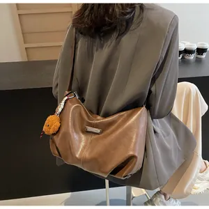 Détail du sac bandoulière en cuir mat marron avec breloque ours et plaque en métal