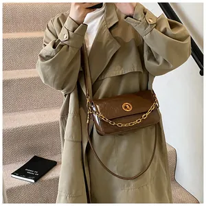 Brown patent leather shoulder bag with gold chain worn by model in a trench coat