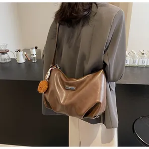 Détail de sac cabas en cuir marron avec surpiqûres blanches et pendentif ours