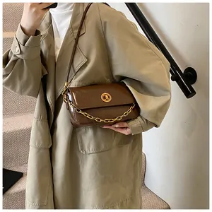 Deep brown glossy leather crossbody bag with bold gold chain shown on a trench coat model