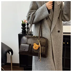 Detail of dark brown leather underarm bag featuring utility pockets and a plush bear charm