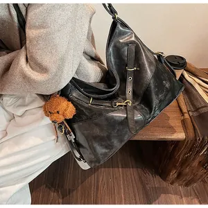 Détail d'un grand cabas noir en cuir vintage avec un pendentif ours et des boucles en bronze