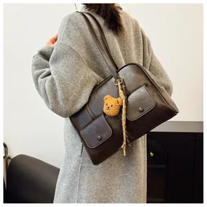 Detail of dark brown vintage shoulder bag featuring side pockets and a cute bear charm