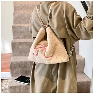 Zaino di peluche beige con fiocco rosa e dettaglio catena indossato da una modella