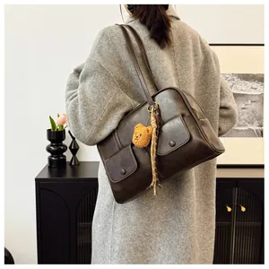 Detail view of coffee leather shoulder bag with front flap pockets and plush bear charm
