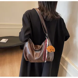 Détail du sac Hobo marron avec breloque chiot en peluche et logo en métal sur la bandoulière
