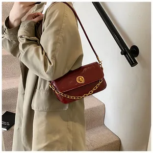 Detail of wine red glossy leather shoulder bag with gold hardware on a trench coat model