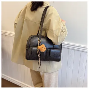 Detail of a vintage black shoulder bag with dual pockets and a cute plush bear charm