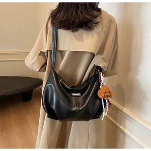 Détail d'un sac plissé noir avec plaque argentée et charm de petit chien en peluche