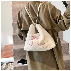 Borsa tote in peluche bianca con ricamo a fiocco rosa e tracolla a catena indossata