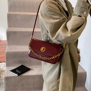 Burgundy faux leather shoulder bag with gold chain and strap shown on beige trench coat