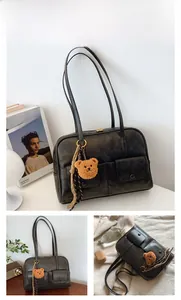 Detail of black retro shoulder bag with dual front pockets and plush bear charm