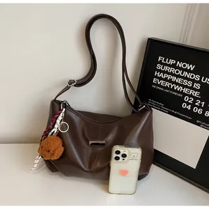 Détail du sac bandoulière marron avec plaque métal, breloque ours et téléphone de référence