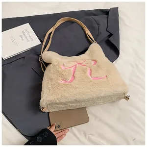 Dettaglio borsa tote in peluche beige con fiocco rosa ricamato accanto a un telefono cellulare