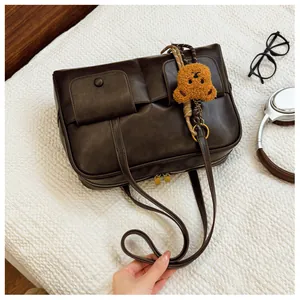Detail of dark brown PU leather tote bag with front flap pockets and bear charm