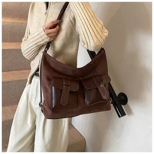 Detail view of dark brown oversized tote bag with dual buckled front pockets and mixed textures