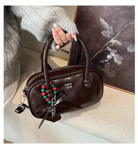 Detail of dark brown glossy pillow bag with silver brand logo and decorative charms