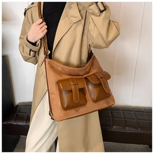 Detail of a brown suede and leather crossbody bag with dual front pockets on a bench