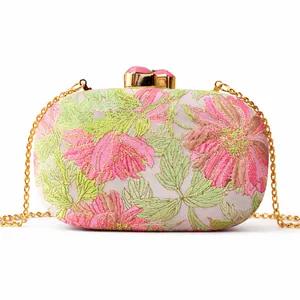 Close-up of elegant floral embroidery and gold metal clasp with pink gemstones on evening bag
