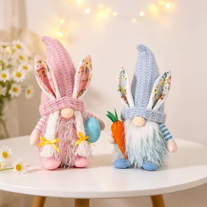 Pair of plush Easter gnomes with bunny ears holding a blue egg and a carrot on white table