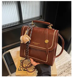 Detail of vintage brown leather handbag featuring gold lettering and baseball keychain