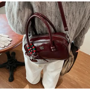 Detail view of burgundy patent leather Boston bag with metal logo and beaded charm decor