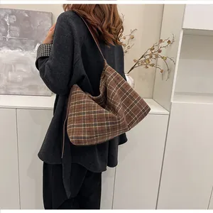 Détail d'un sac cabas à carreaux marron porté par un mannequin dans un décor épuré