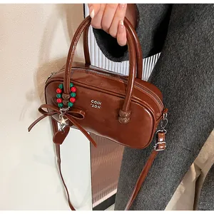 Detail of a dark brown crossbody bag featuring red and green bead charms and metallic logo