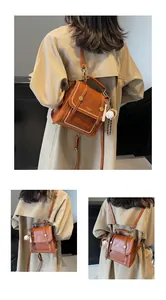 Detail view of a vintage brown leather backpack with pearl studs and a baseball charm