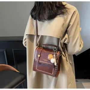 Detail of brown vintage crossbody bag featuring white stitching and baseball glove charm