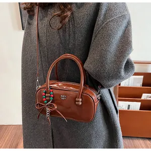 Detail of glossy brown patent leather crossbody bag with metal logo and charm accessory