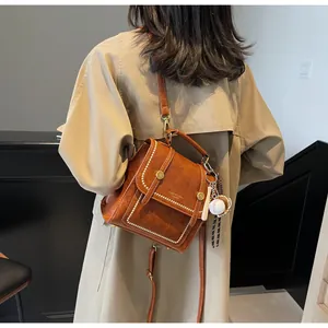 Detail of caramel brown retro shoulder bag with white topstitching and baseball charm