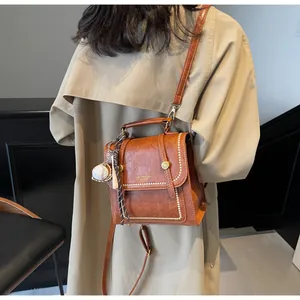 Brown retro mini handbag with baseball pendant shown on beige coat back view