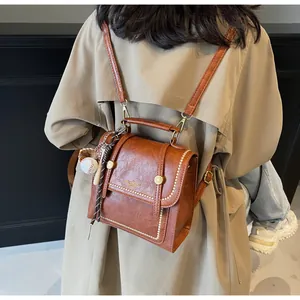 Detail of brown retro handbag with white stitching and baseball charm on a model