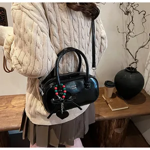 Glossy black leather handbag featuring dual handles and heart pendant in a cozy winter setting