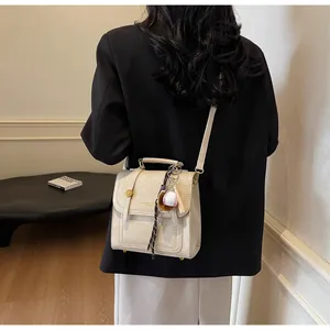 Detail of cream white textured handbag featuring a gold buckle and baseball charm
