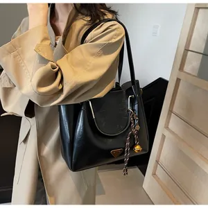 Detailed view of black PU leather tote with gold hardware and woven bell ornament charm
