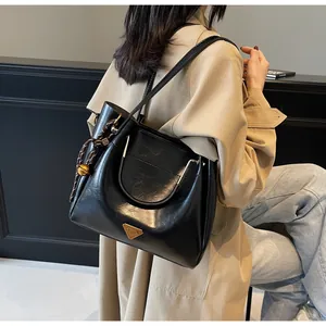 Detail of black tote bag with golden triangle logo and woven ball charm on a beige coat