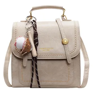 Chic beige faux leather handbag with wavy stitching and baseball charm on white background