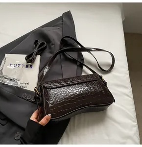 Detail der dunkelbraunen Tasche mit Krokodilmuster und goldfarbenen Metallschnallen