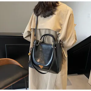 Close-up of black glossy tote bag with gold hardware and adjustable strap on model