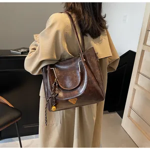Detail of a dark brown vintage tote bag with metal triangle plaque on a khaki coat