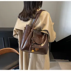 Detail of dark brown tote bag with vintage leather texture and gold bell pendant